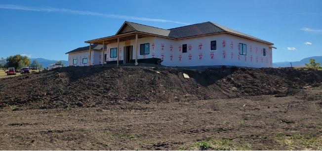 Single-story house under construction on a dirt hillside under a clear blue sky