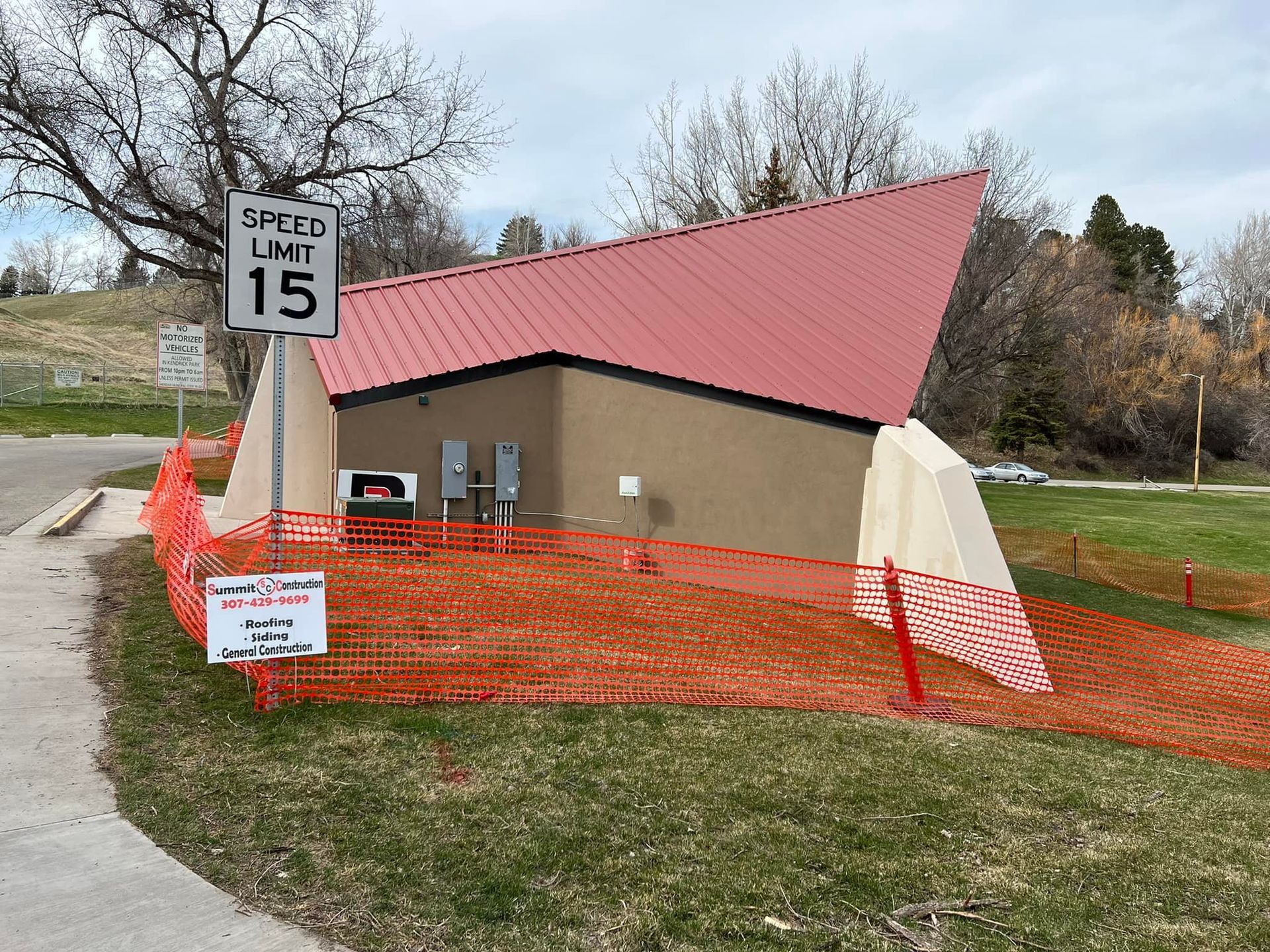 Small building with red roof behind orange safety fencing and a speed limit 15 sign on a grassy roadside.