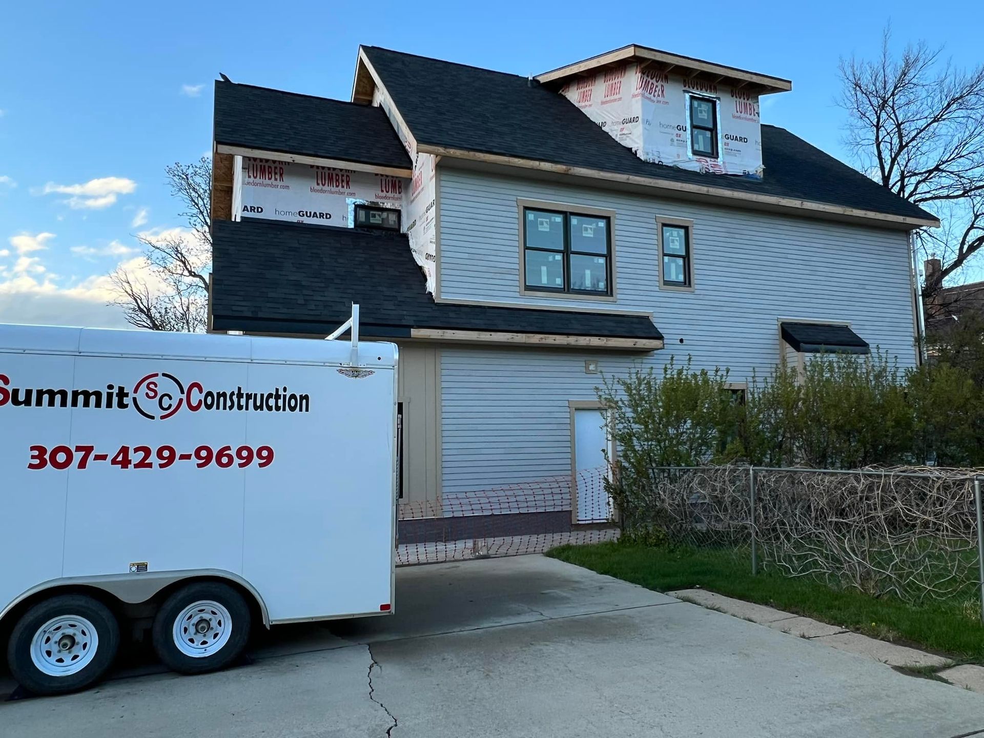 Construction trailer parked beside a damaged house with boarded windows and peeling siding
