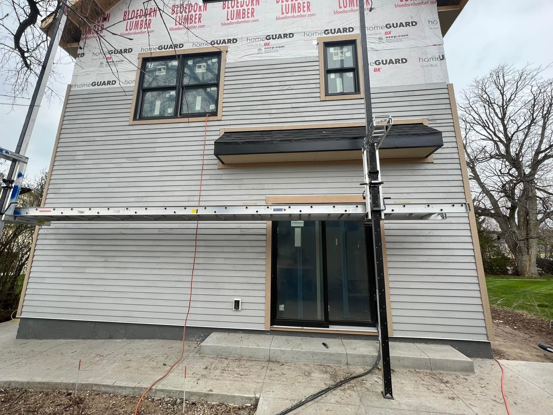 Two-story gray house exterior under construction, with windows, siding, and a front door.