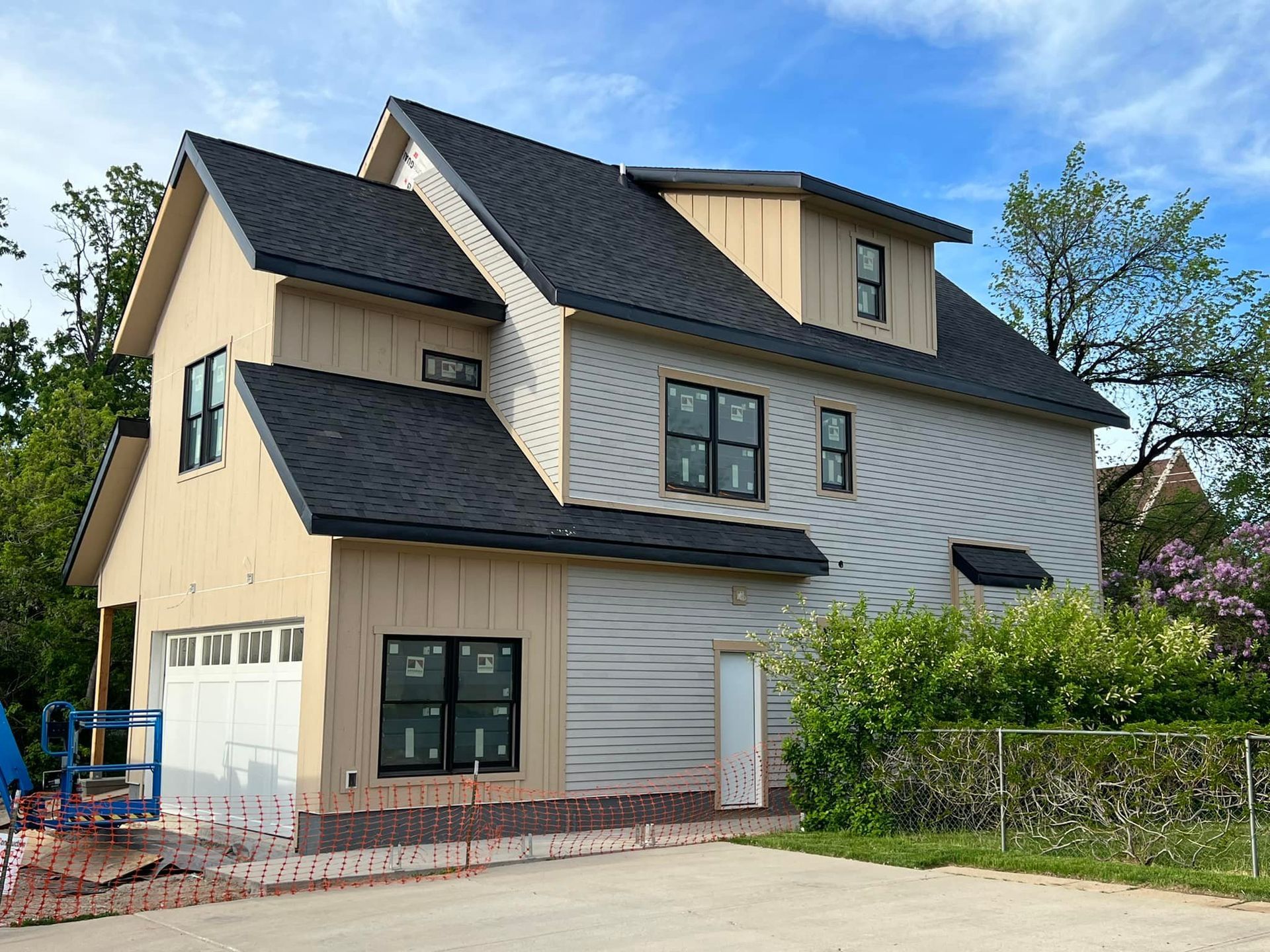 Two-story beige house with black roof and white-trimmed windows under a blue sky