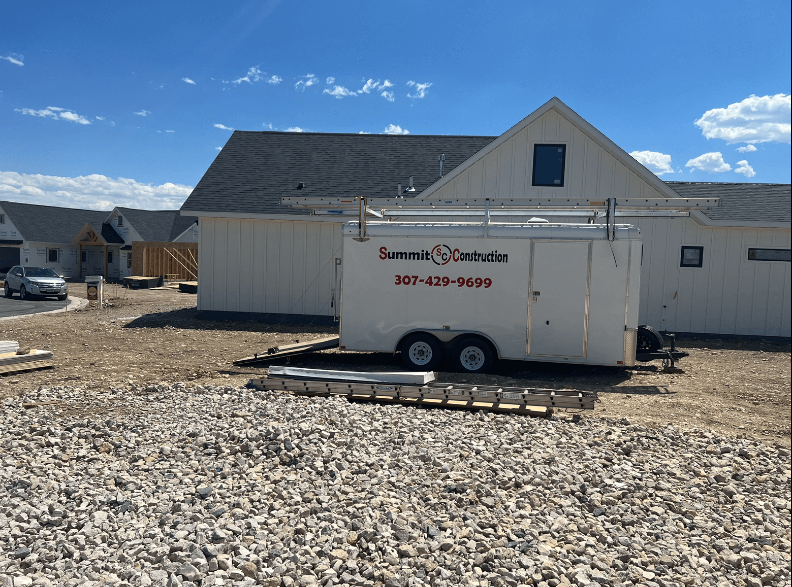 White utility trailer parked beside a house on a gravel lot under a bright blue sky