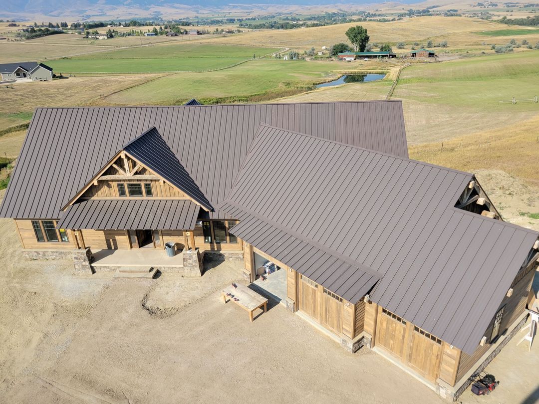 Aerial view of a large wooden house with a dark roof in a dry rural landscape.