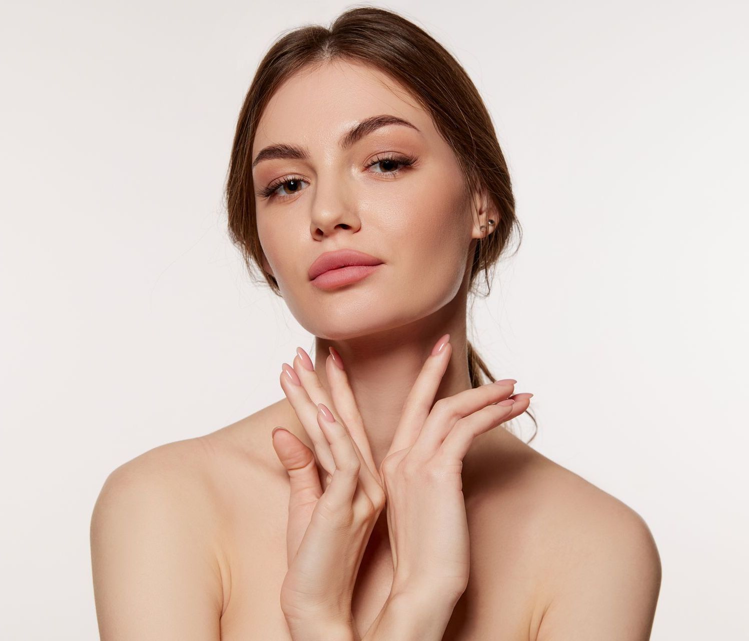Portrait of a woman with hands near her neck against a plain white background