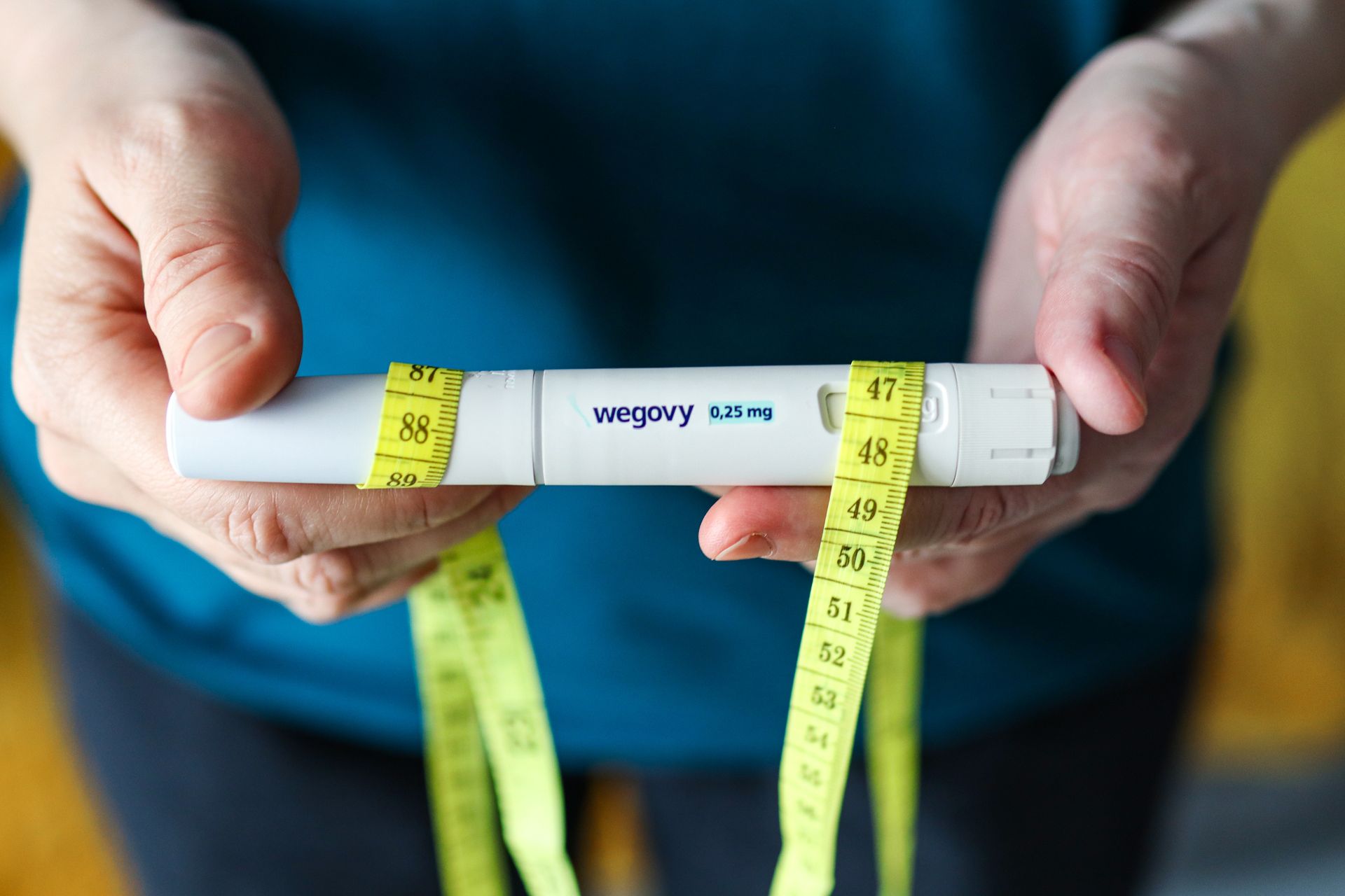 Hands holding a white inhaler with yellow measuring tape wrapped around it