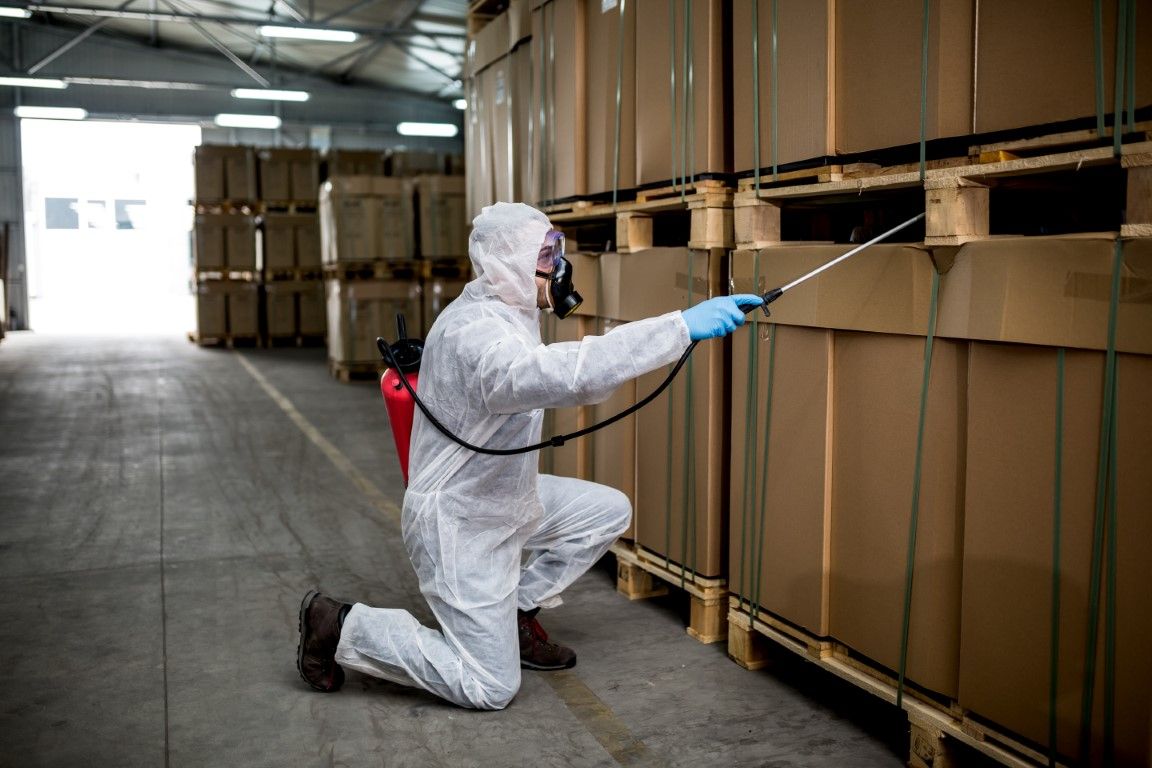 Worker in white protective suit inspecting stacked cardboard boxes in a warehouse