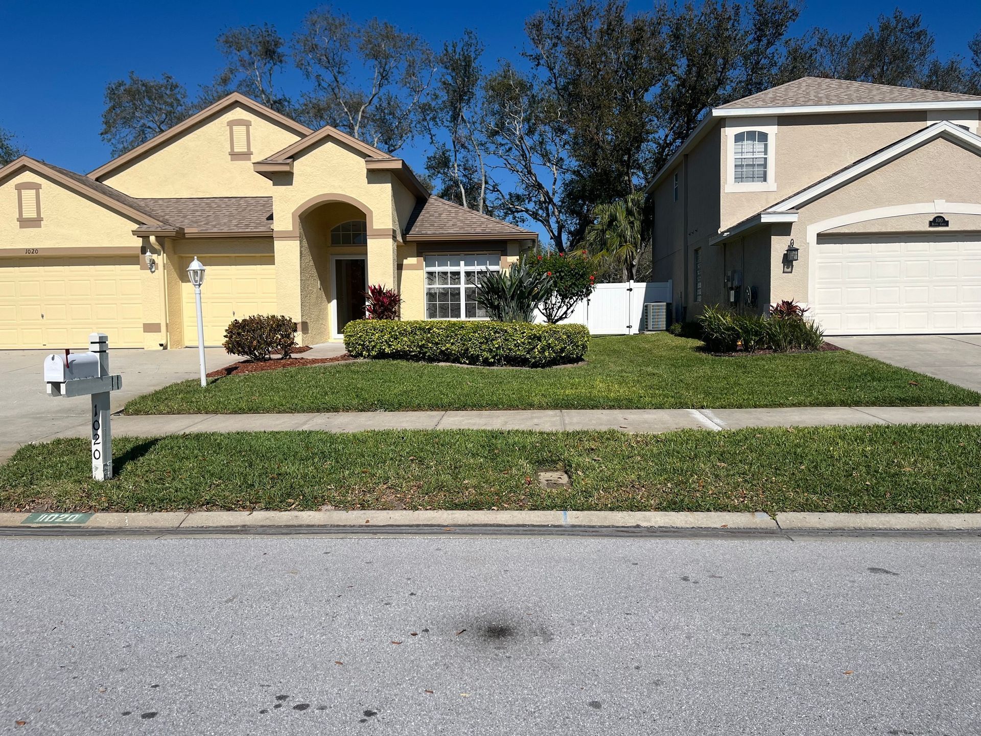 Two suburban single-story homes with yellow stucco exteriors, garages, and landscaped front lawns under a clear blue sky.
