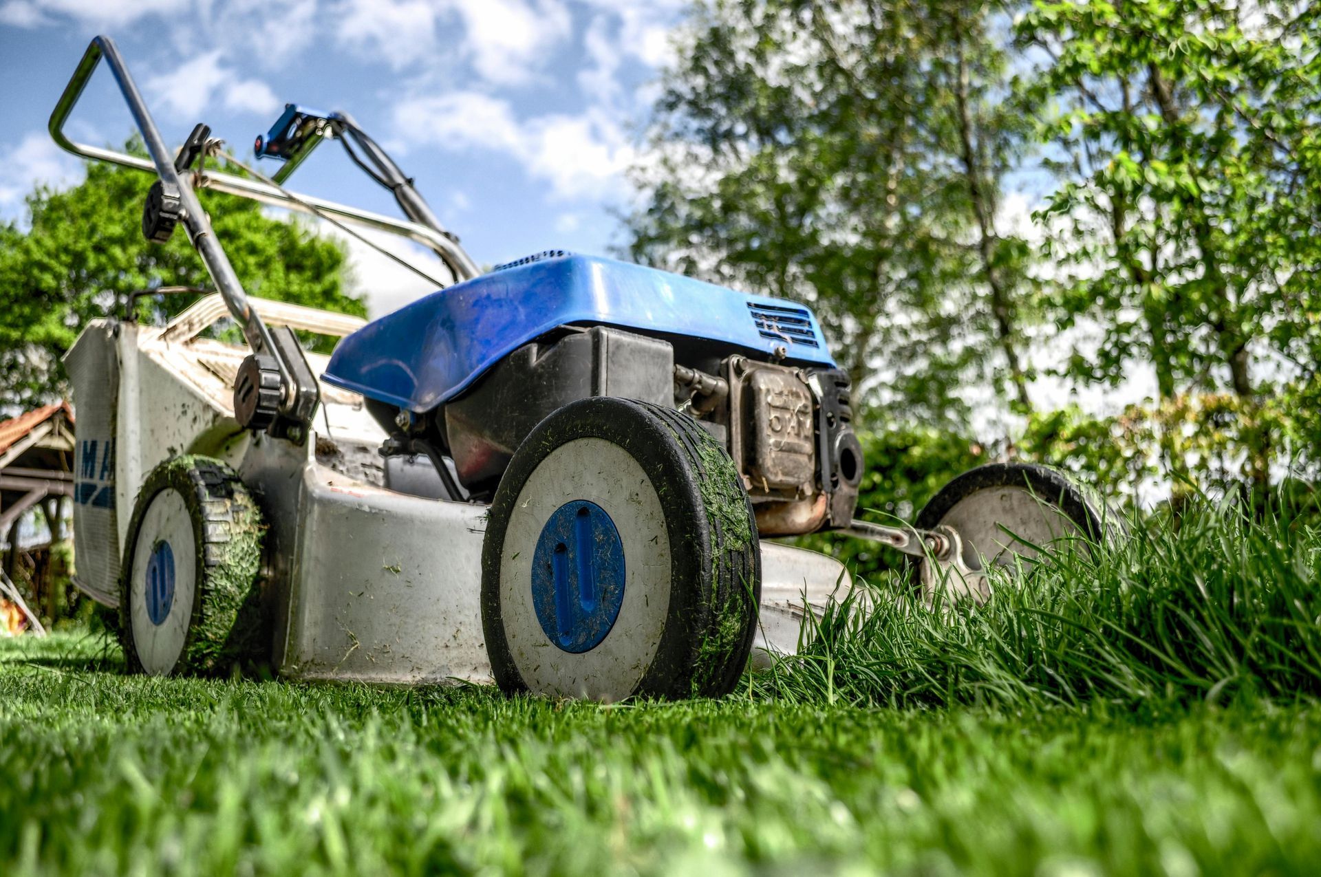 A blue and white lawn mower sitting on a freshly cut, green grassy lawn under a sunny, partly cloudy sky.