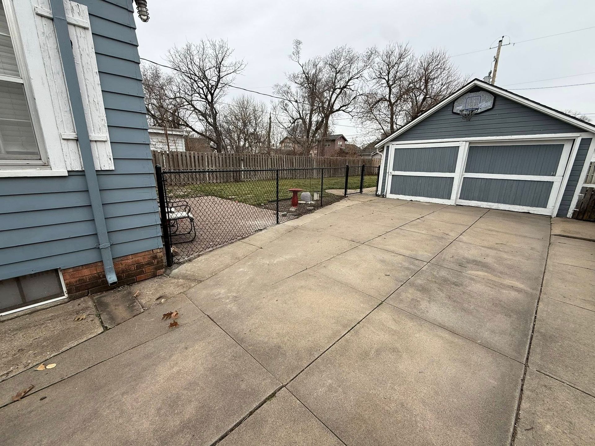 A blue-sided house with a concrete driveway leading to a matching blue garage, bordered by a black fence and yard.