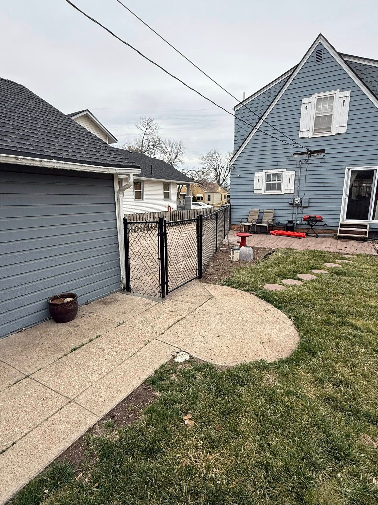 A gravel patio leads to a black gate between a blue garage and a blue house with white trim.