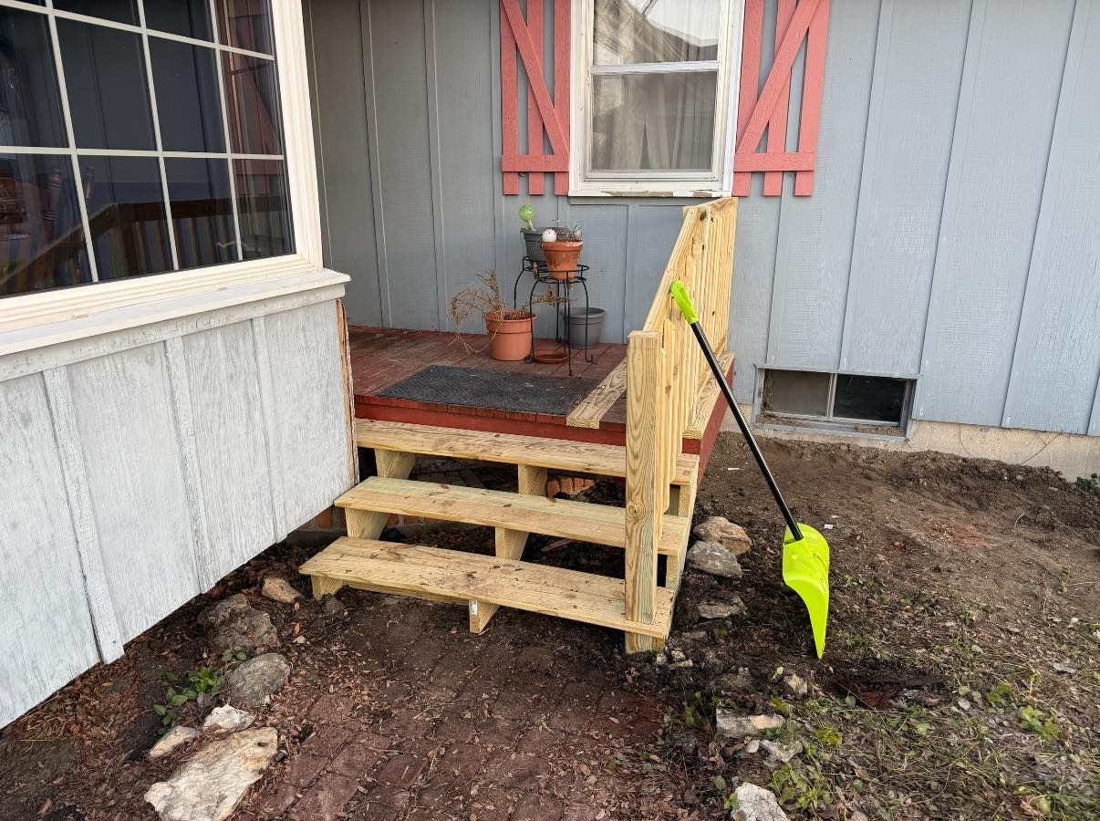 New wooden stairs leading to a small porch, with a bright green garden shovel leaning against the side.