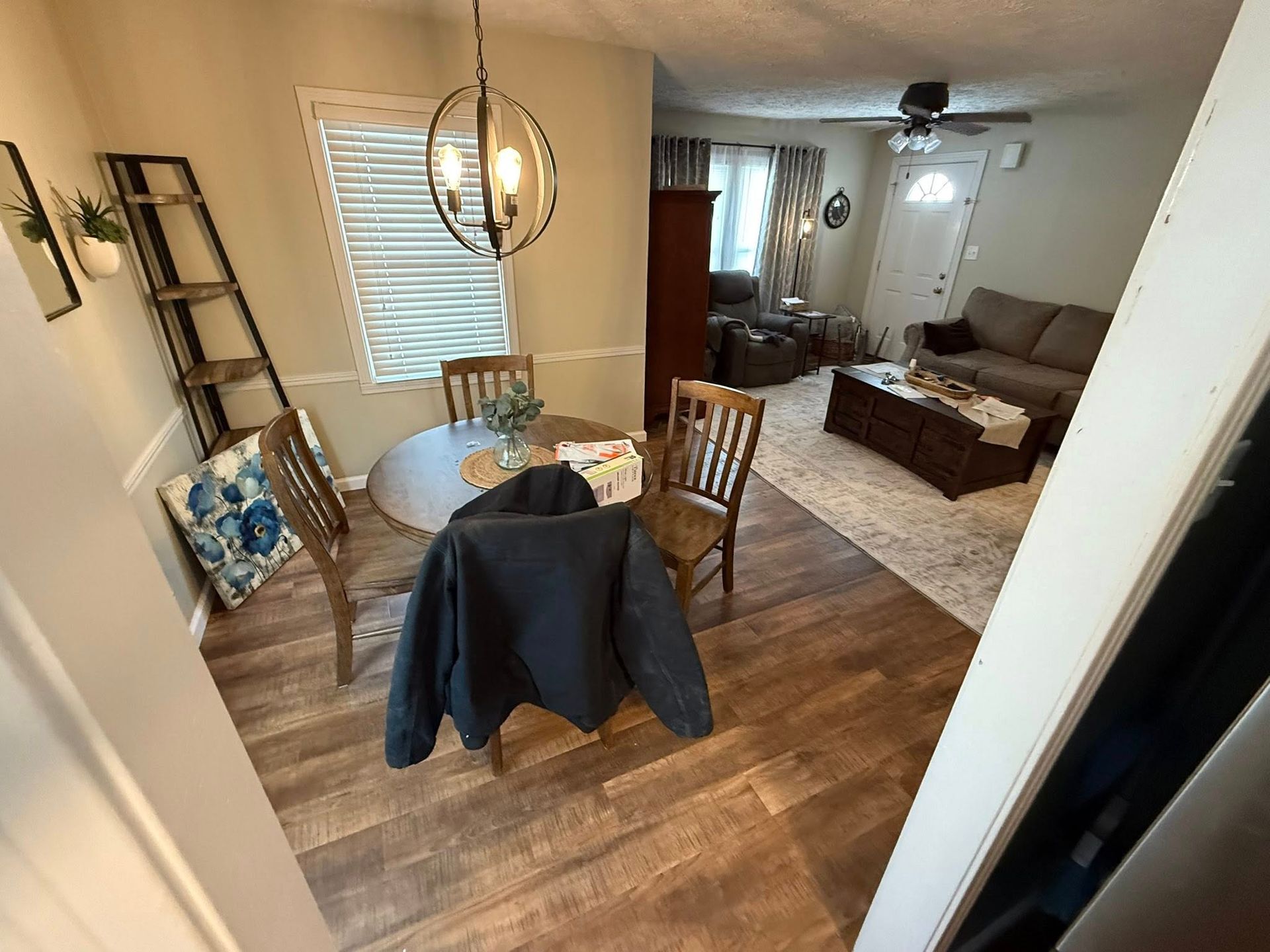 A dining area with a round wooden table and chairs leads into a living room with a sofa, coffee table, and area rug.