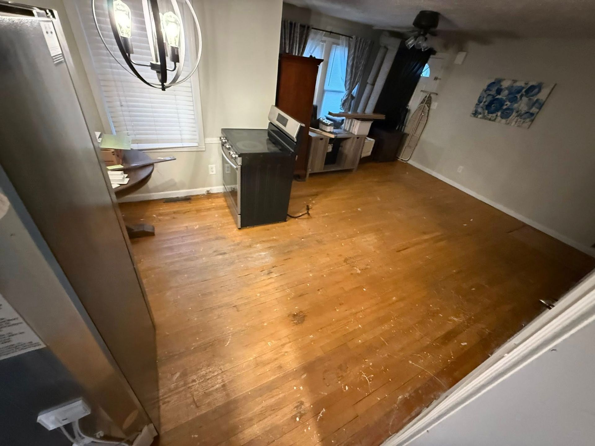 An empty, open-plan room with hardwood floors, a black stove, a round wooden table, and a hanging light fixture.