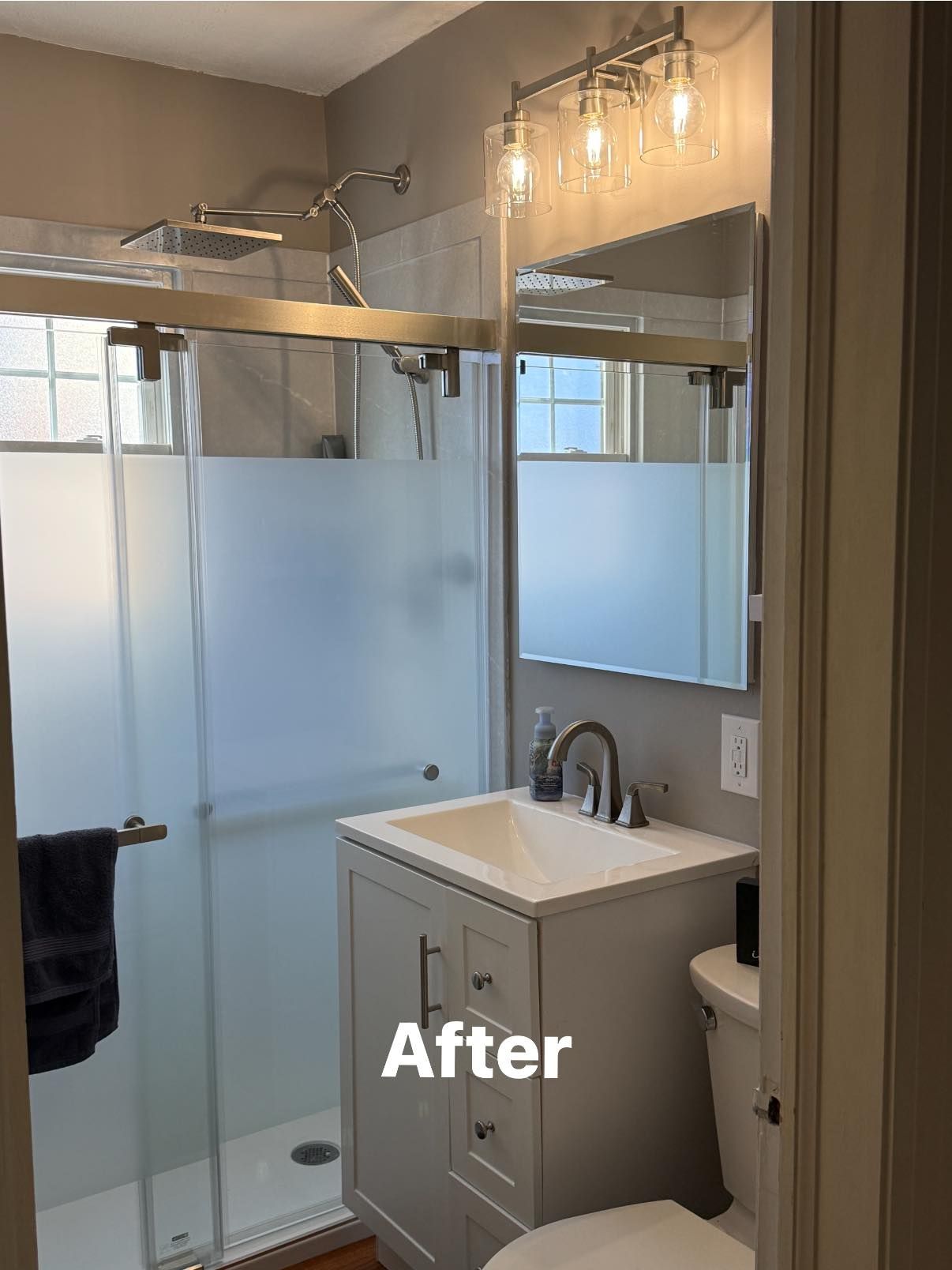 A renovated small bathroom featuring a gray vanity, a glass-enclosed shower, a wall mirror, and modern vanity lighting.