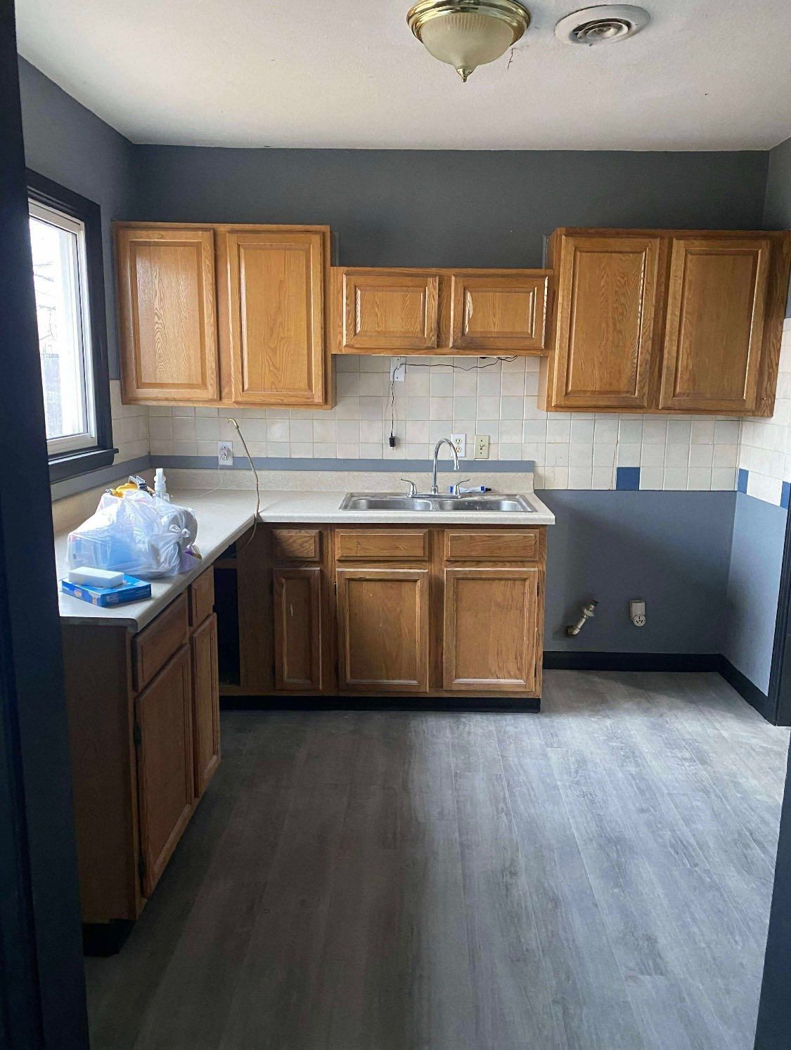 Kitchen with oak cabinets, grey walls, white tiled backsplash, and light grey wood-look flooring.