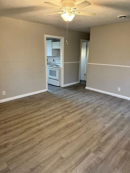 Empty living room with light brown walls, a white chair rail, light wood-look floors, a ceiling fan, and open doorways.