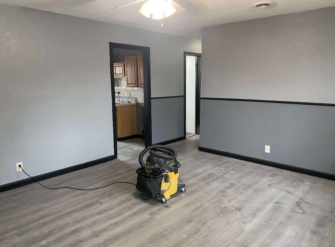 A room with gray walls, a black chair rail, wood-look flooring, and a yellow shop vacuum sitting in the center.