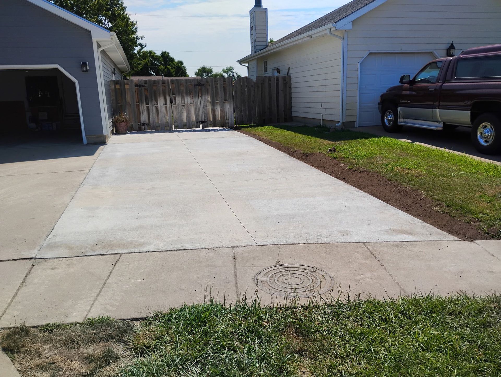 A newly poured concrete driveway between a gray garage and a light-colored house with a parked truck.