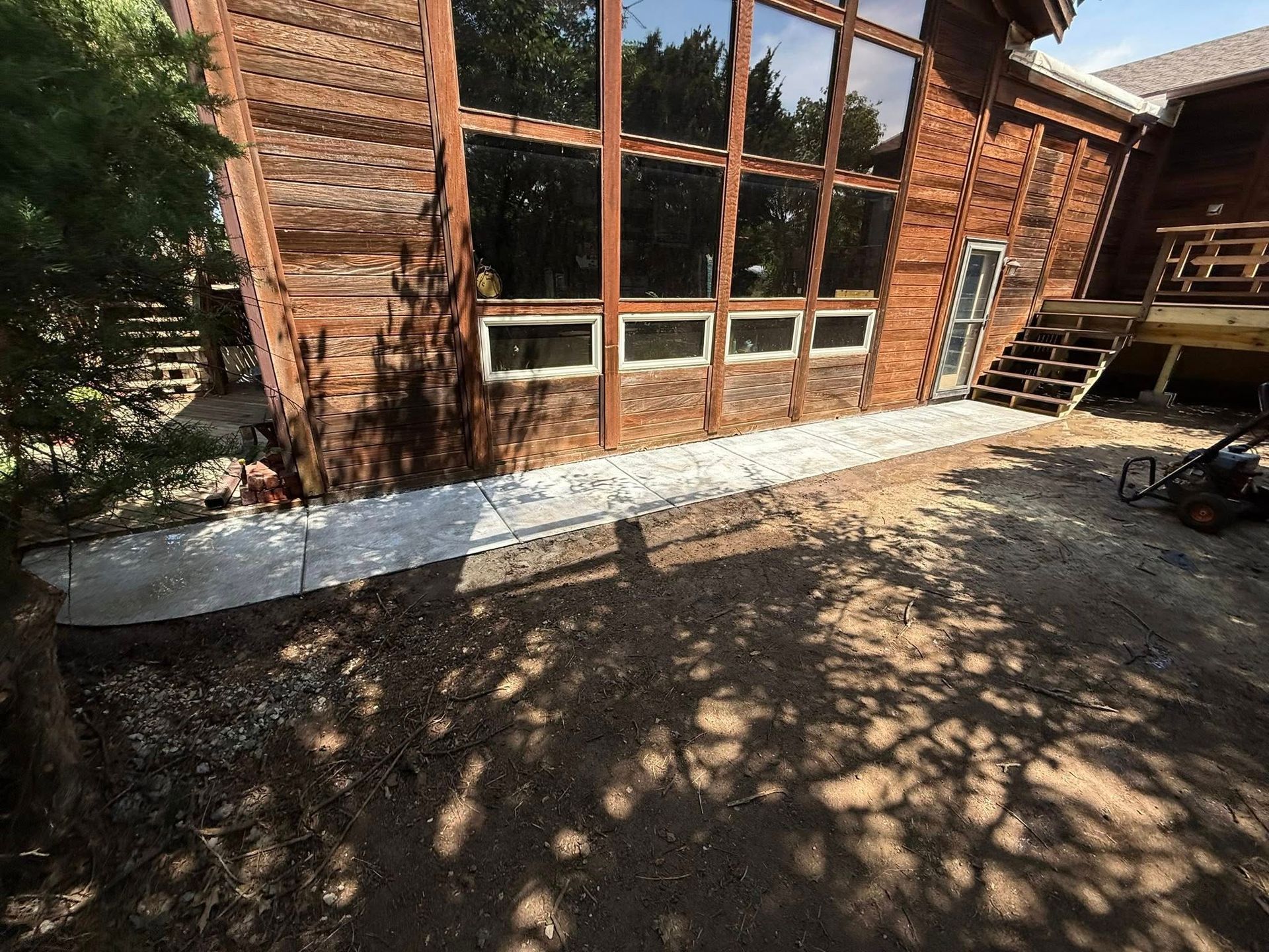 A stone walkway runs along the side of a large rustic wooden cabin with tall glass windows and a wooden deck.
