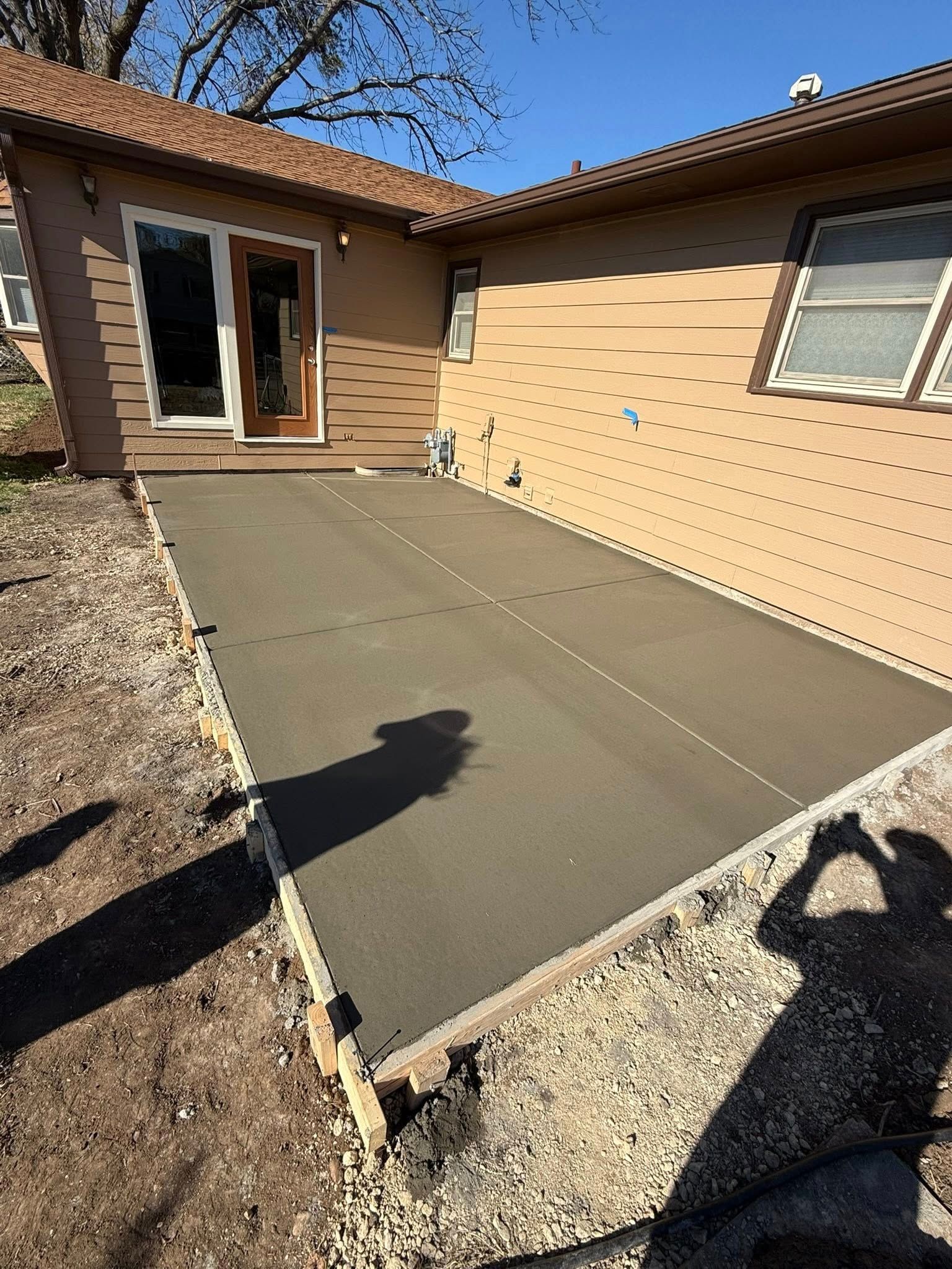 A newly poured rectangular concrete patio area against the side of a tan house on a sunny day.