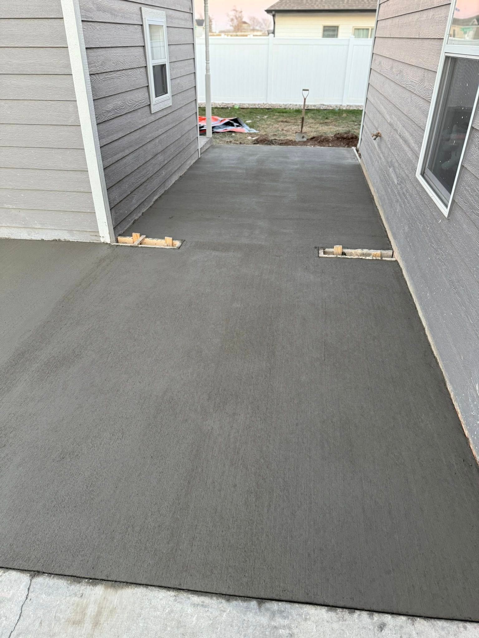 A newly poured gray concrete driveway located between two light gray houses with white trim.