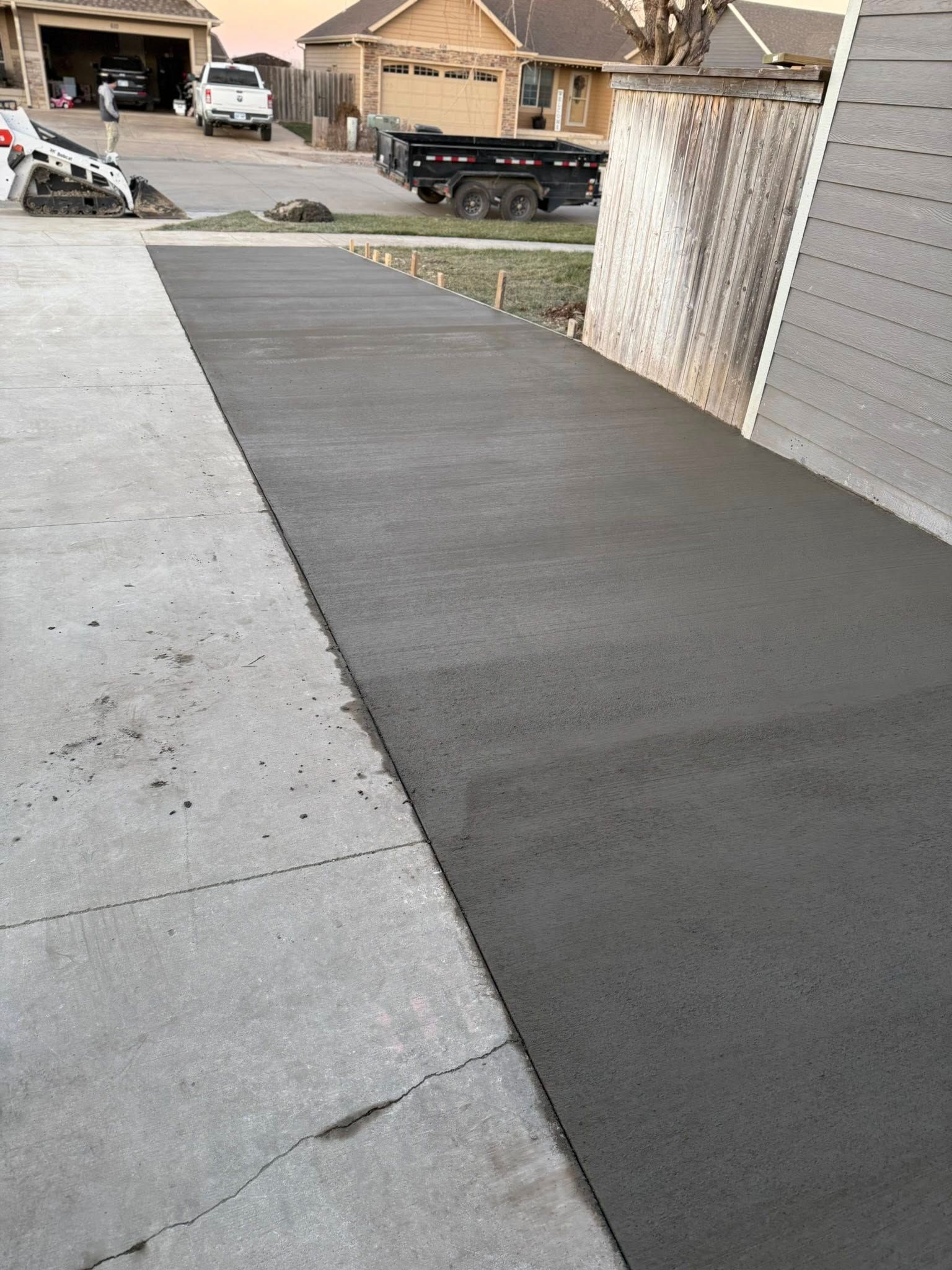 A newly poured dark concrete strip bordering an existing driveway in a residential neighborhood.