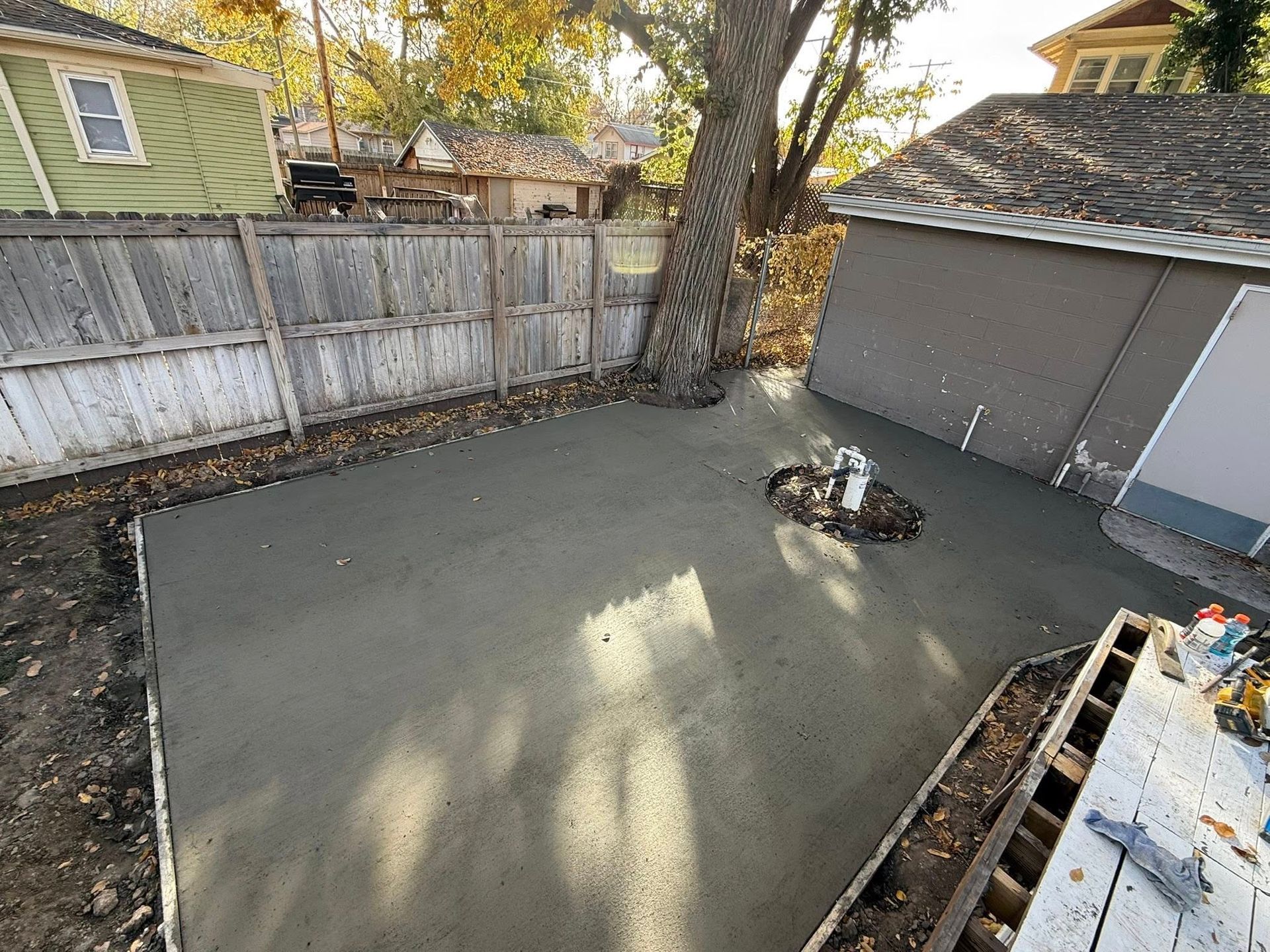 Freshly poured concrete patio in a backyard, featuring a small circular garden cutout and a wooden fence backdrop.