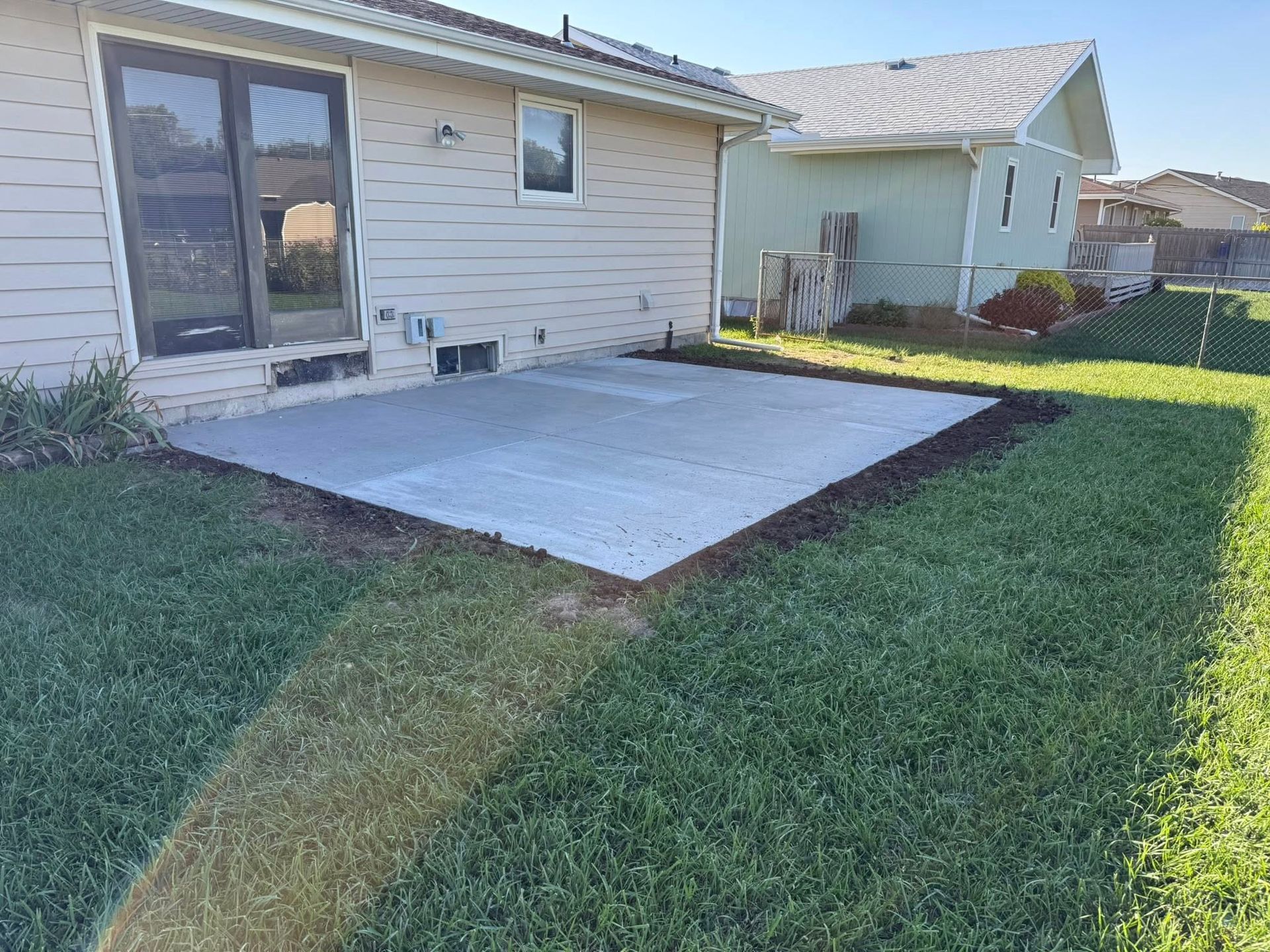 A light-colored house with a newly poured rectangular concrete patio in the backyard on a sunny day.