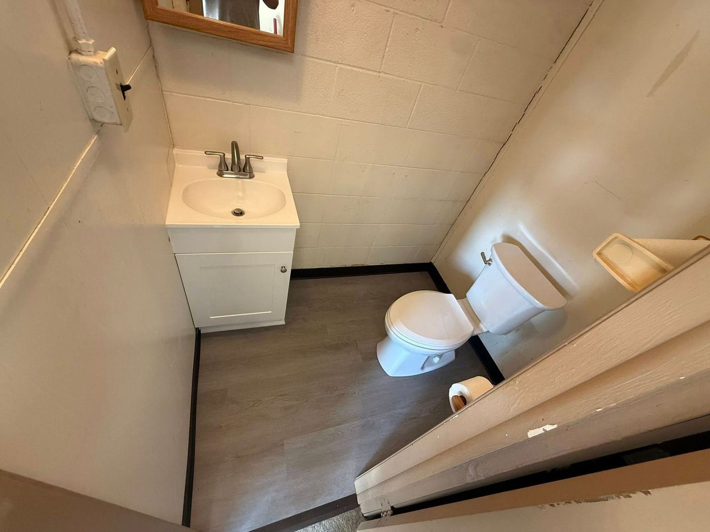 Small bathroom with a white pedestal sink, toilet, and grey flooring against plain, off-white cinder block walls.