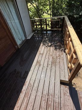 A weathered outdoor wooden deck with peeling finish, partially in sunlight, adjacent to a house with a sliding door.