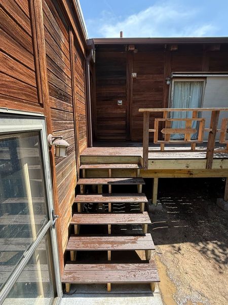 Wooden staircase leading to a wooden deck attached to a rustic brown log cabin with a partial view of a window.