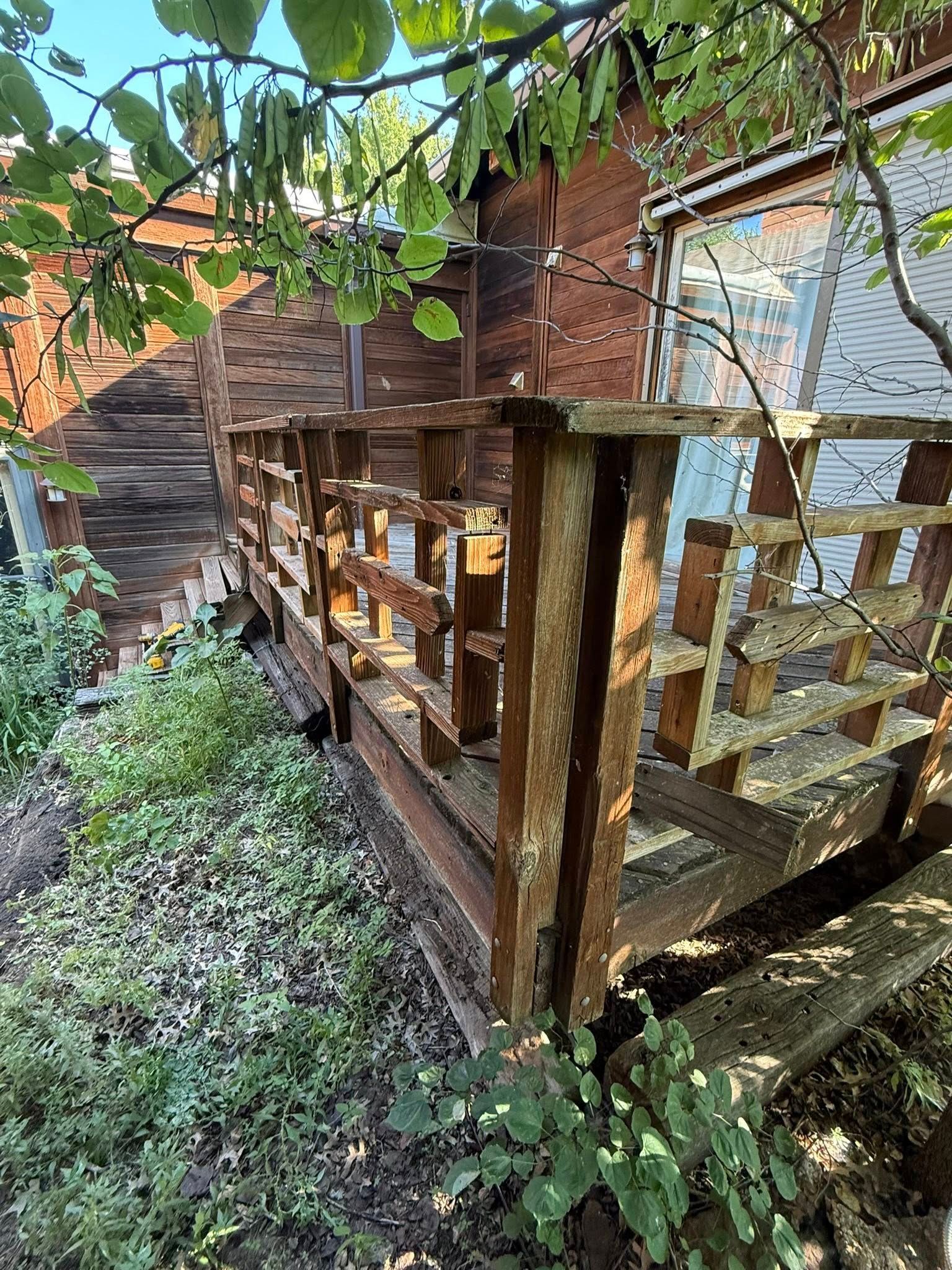 An elevated wooden deck with a weathered lattice railing, situated next to a brown building partially shaded by trees.