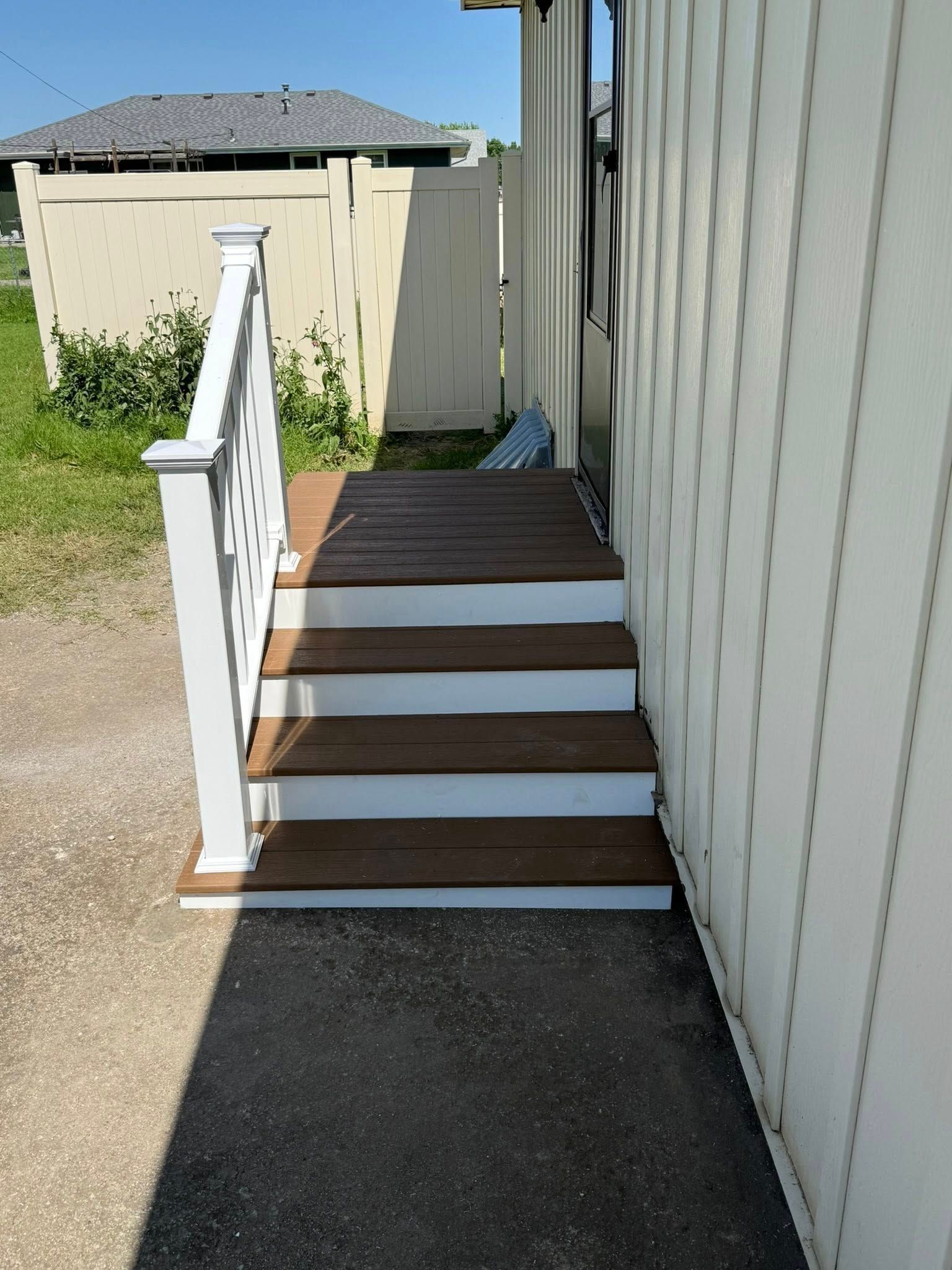 Small outdoor wooden staircase with white railings, leading to a doorway on a house with beige vertical siding.