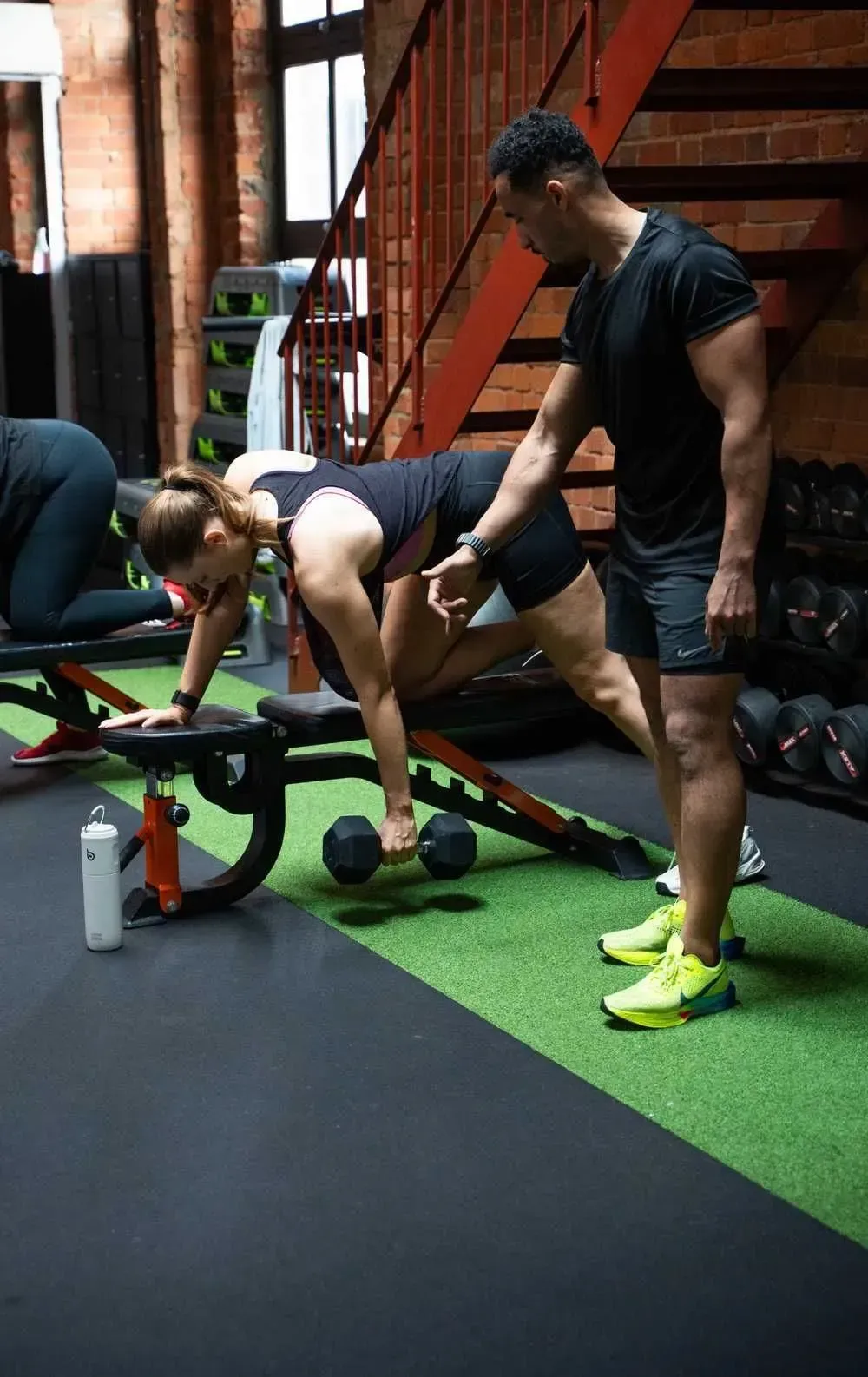 HIIT West Hampstead coach guiding a member through a one-arm dumbbell row