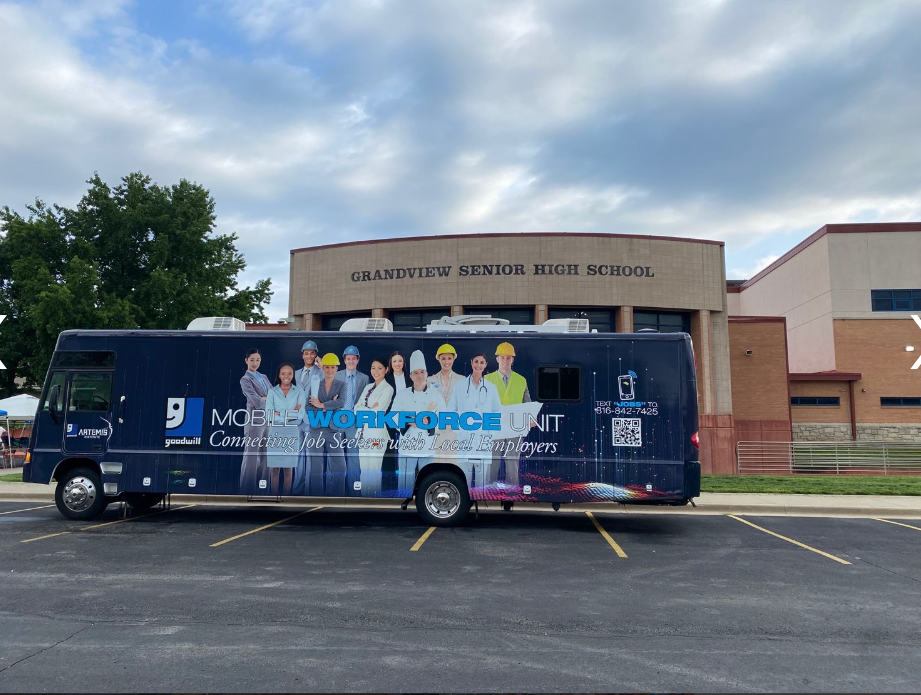 Blue mobile clinic bus parked outside a hospital under cloudy skies
