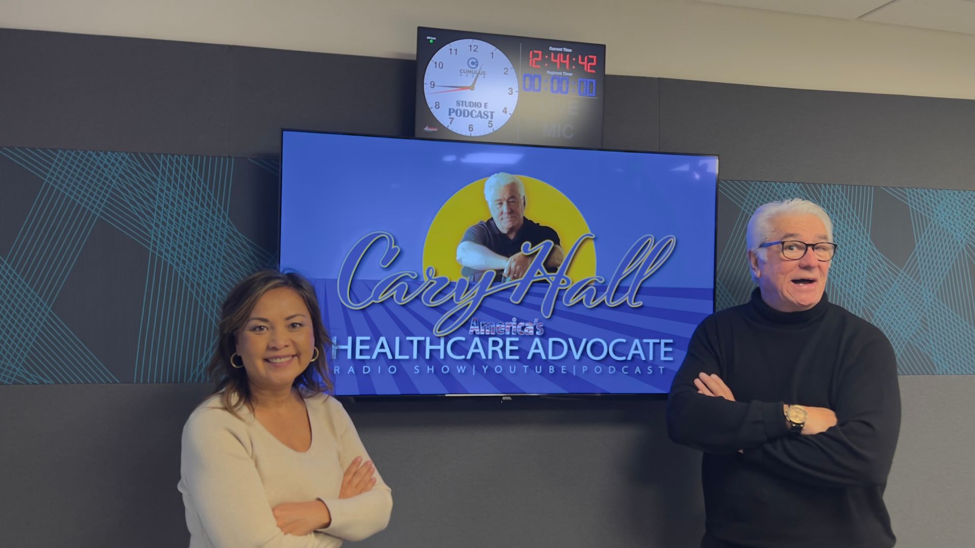 Two people posing in front of a TV screen that reads “Healthcare Advocate”
