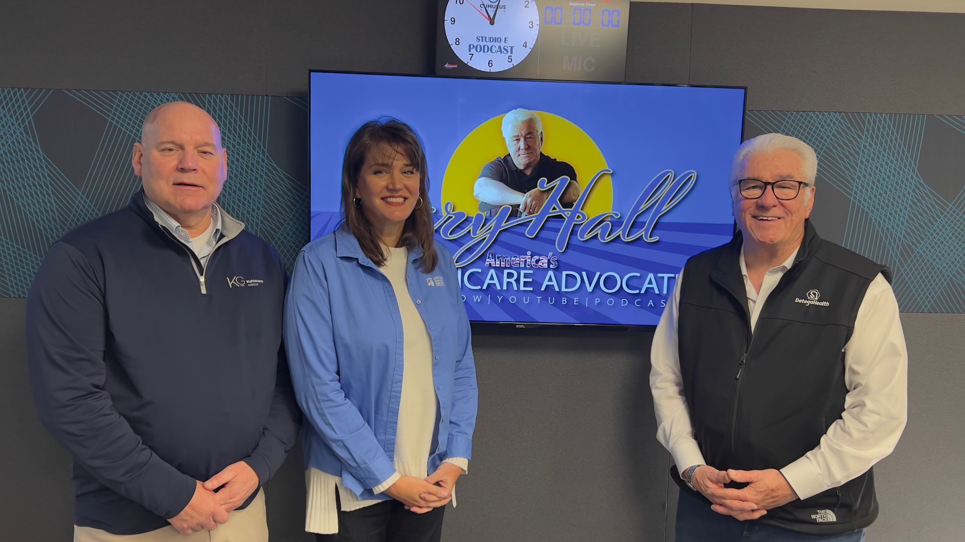 Three people standing indoors beside a Care Advocate sign and clock on a wall