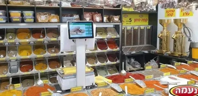 תצוגה בחנות תבלינים עם צנצנות צבעוניות של תבלינים ומשקל דיגיטלי על הדלפק