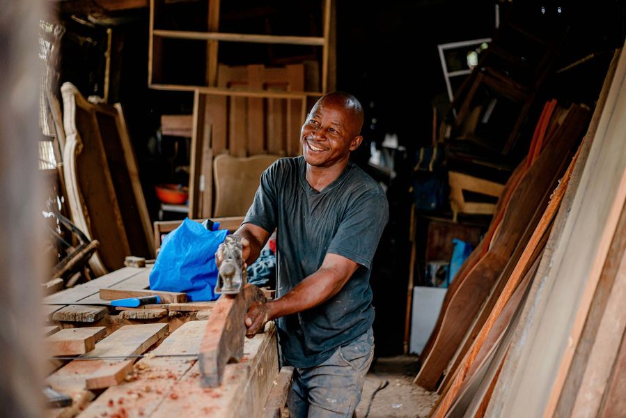Man smiling while using a hand saw in a cluttered woodworking shop