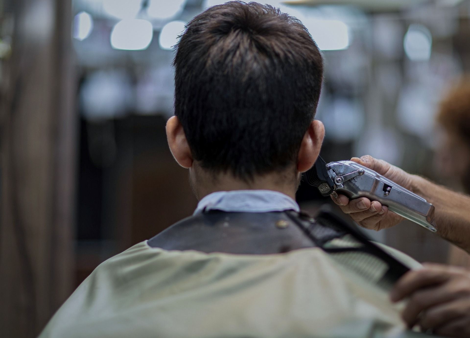 Barber trimming the back of a customer's neck with clippers in a barbershop