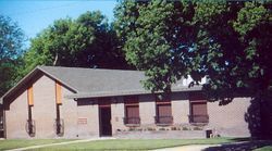 Brick building with brown accents and small windows, surrounded by green trees.