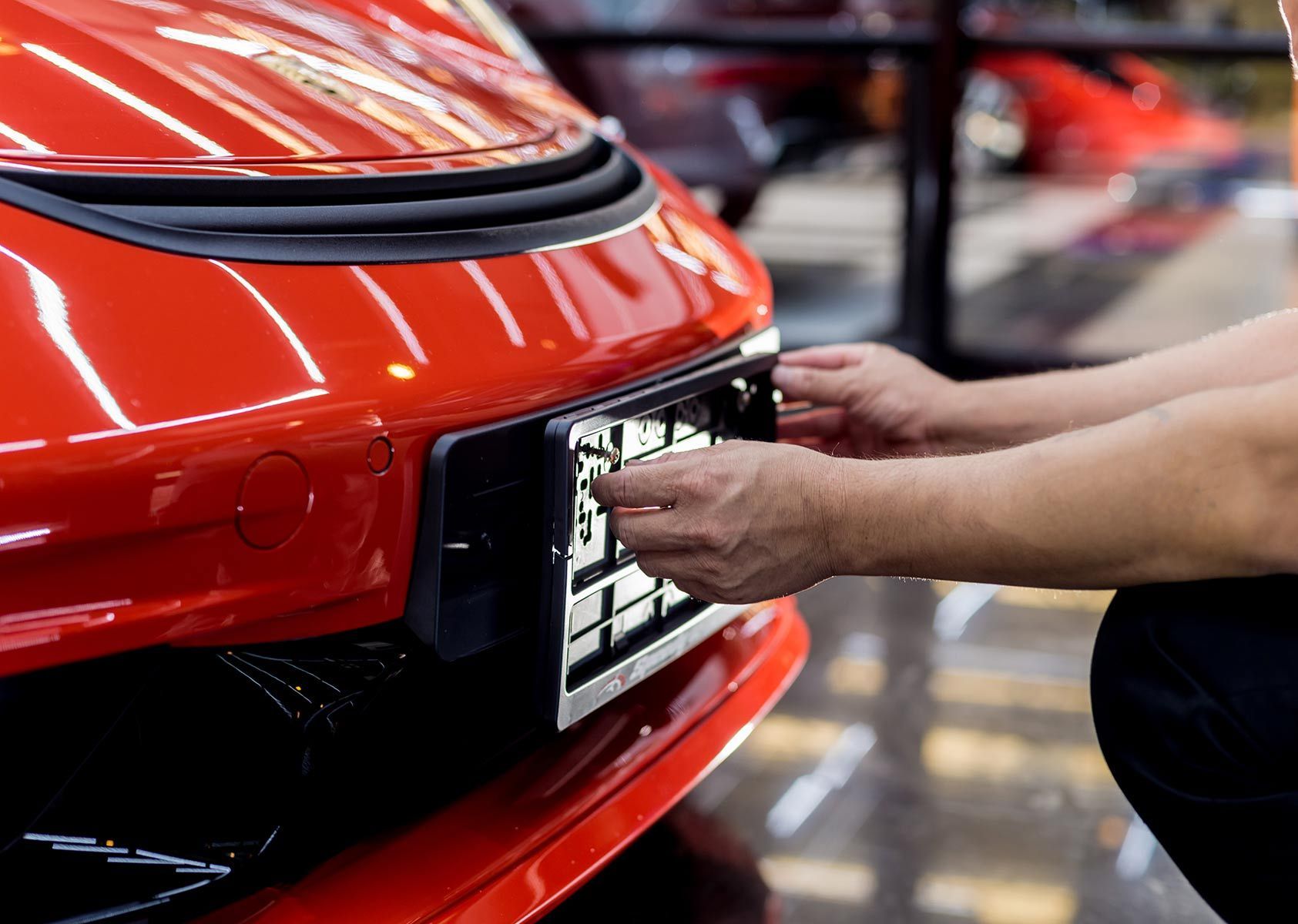 A Man Is Putting A License Plate On A Red Car — Auto Marvel In Mount Saint John, QLD