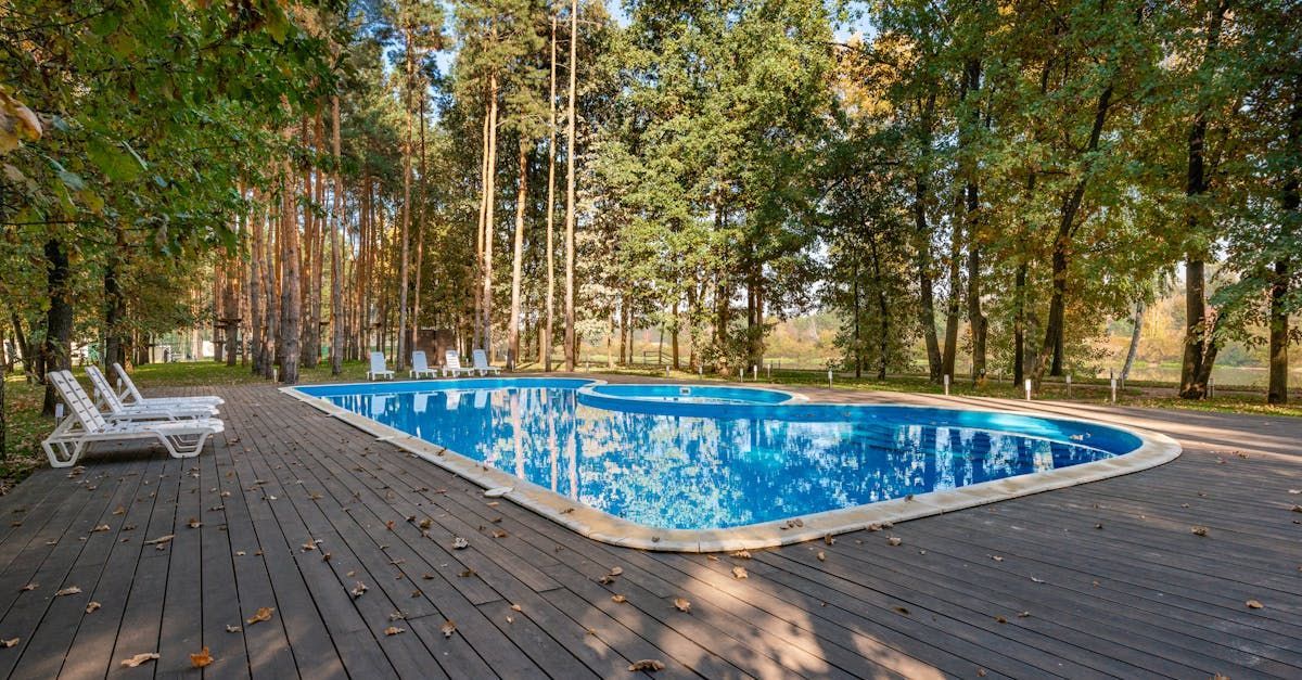 A large swimming pool is surrounded by trees and a wooden deck.