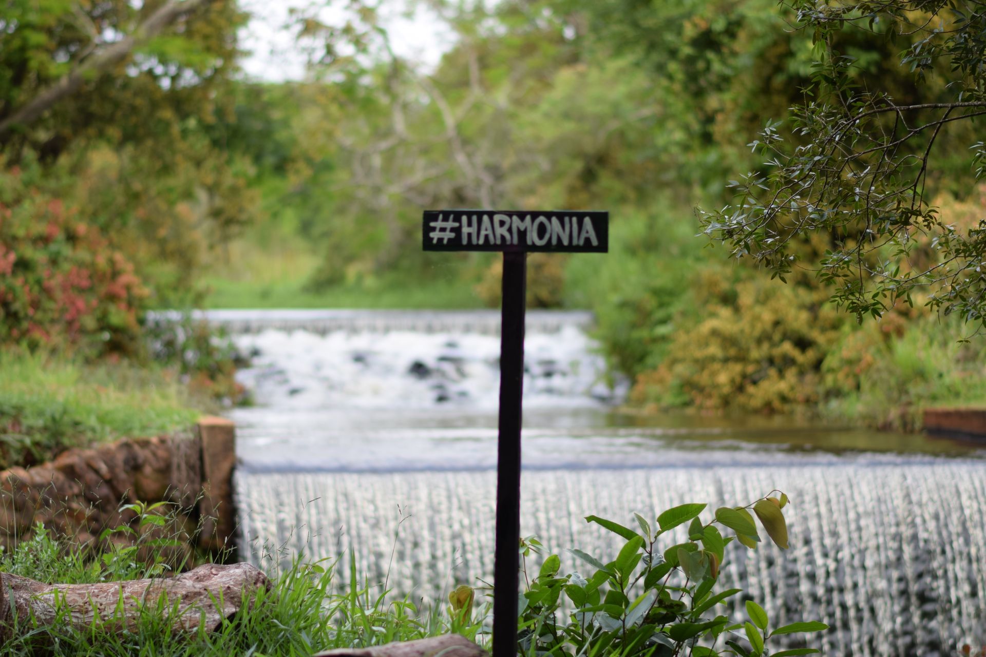 Uma placa em um poste em frente a um rio com uma cachoeira ao fundo.