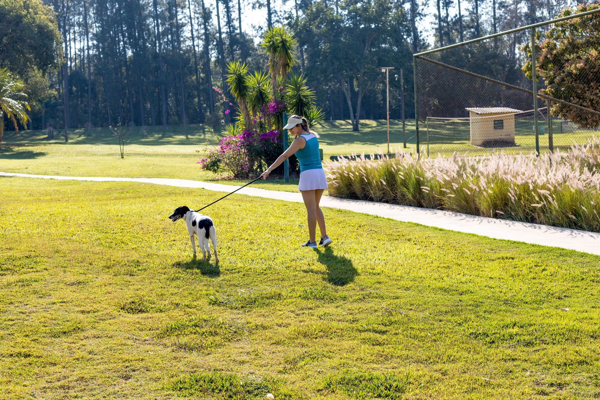 Uma mulher está passeando com um cachorro pequeno na coleira em um parque.