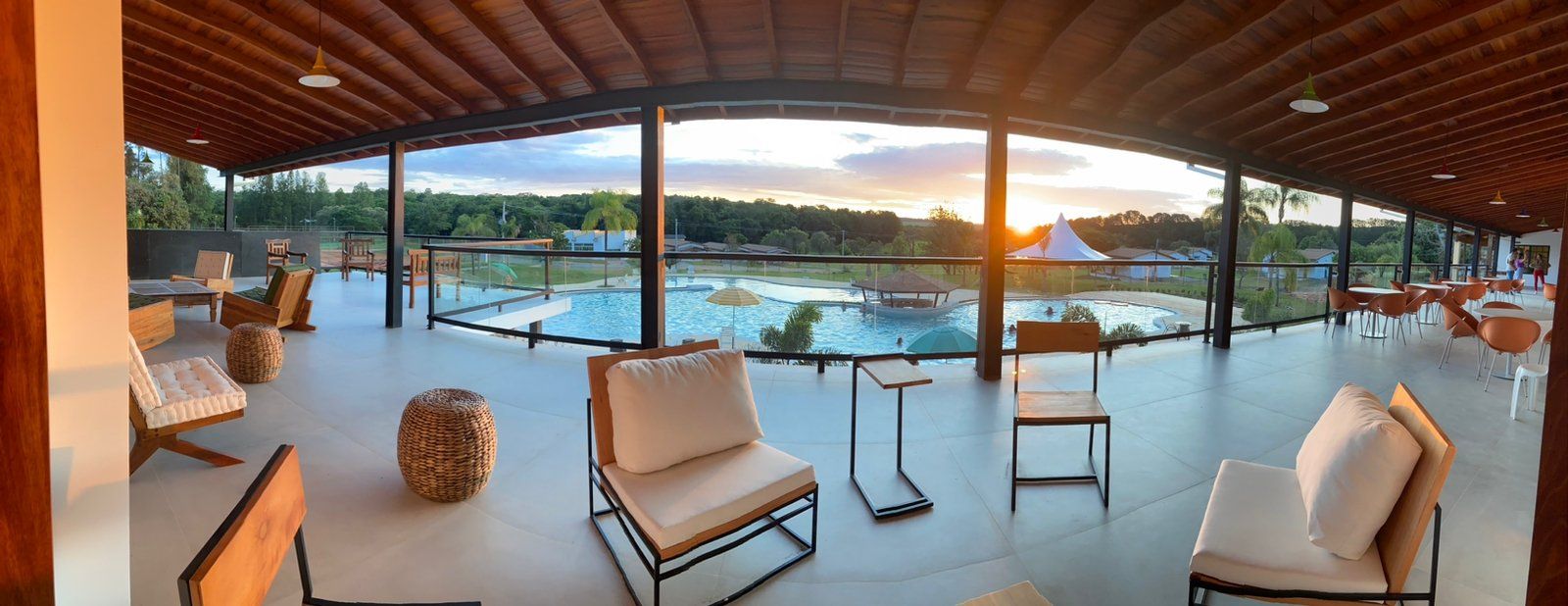 Uma sala grande com cadeiras e mesas e vista para uma piscina ao pôr do sol.