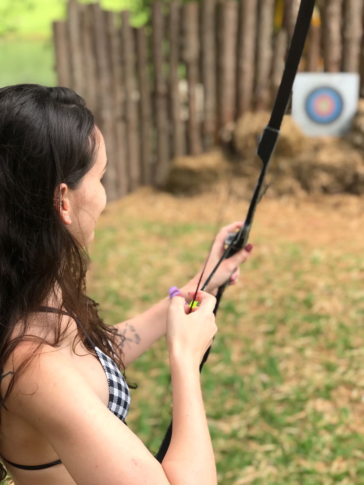 Uma mulher de biquíni está segurando um arco na frente de um alvo.