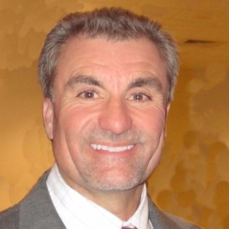 Man in a gray suit smiles at the camera against a neutral background.