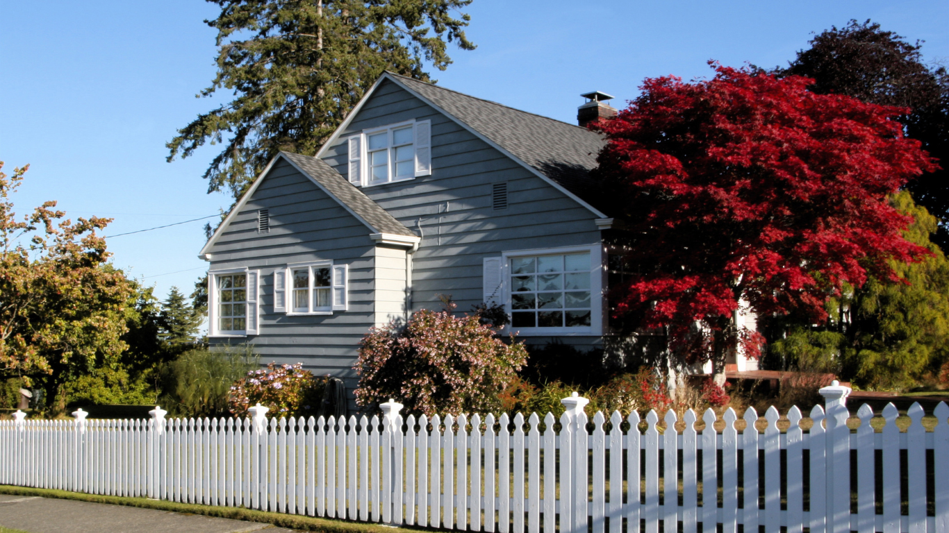 Gray house with white picket fence and red tree in front.