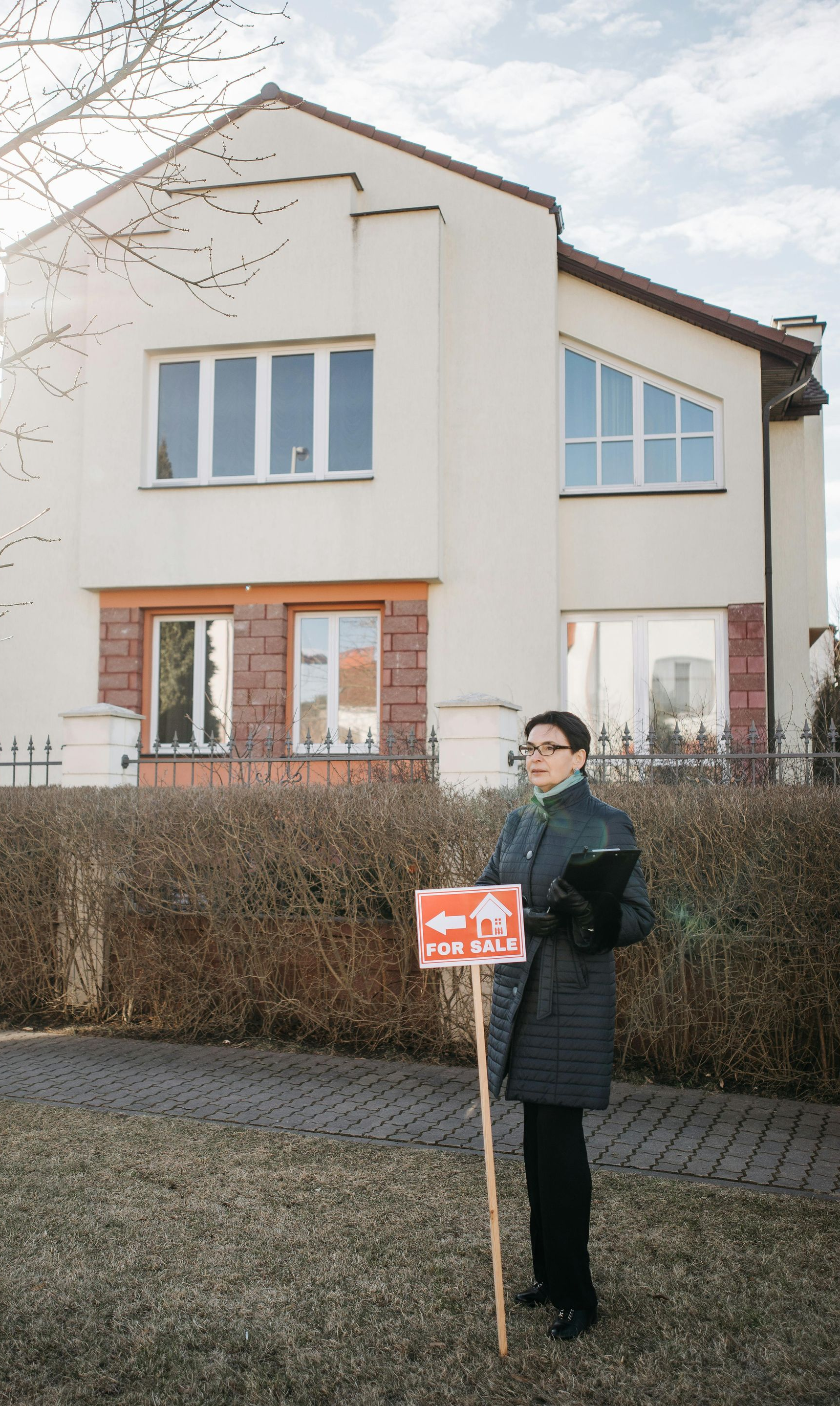 Person holding a directional real estate sign in front of a modern house.